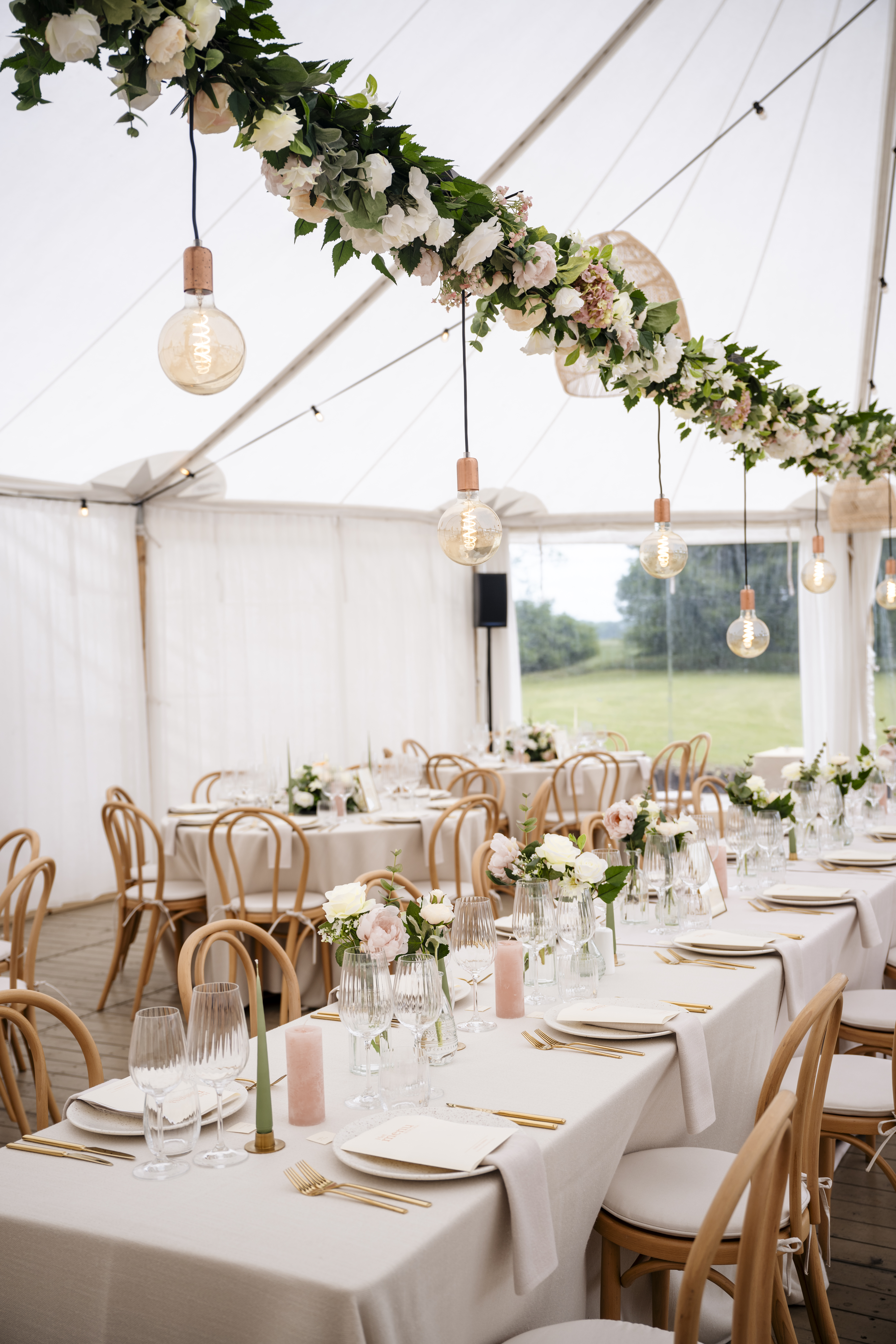 Bruiloftsaankleding op maathandgemaakte bloemenslinger van zijden bloemen Tafelaankleding met zijden bloemen tijdens bruiloft in tent, met lange bloemenslinger in de lucht, ontworpen door Yacintha van Zijden Bloemen Service.